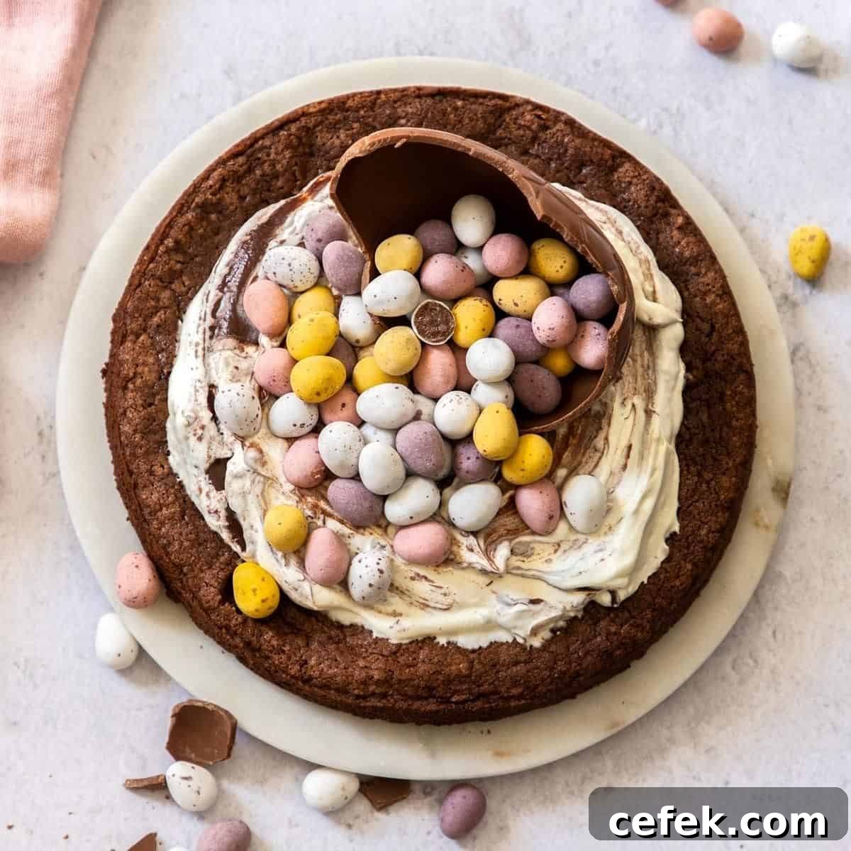 Whole cake sitting on a plate, decorated with cream and Easter chocolates.