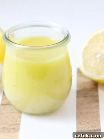 Lemon garlic salad dressing in a glass jar on a white and wooden board with fresh lemon halves and garlic.