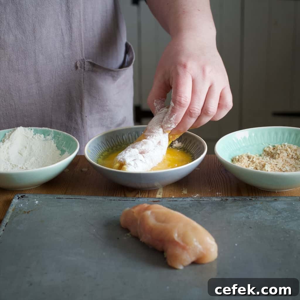 Woman's hand rolling a rolled chicken breast into a small bowl of beaten eggs