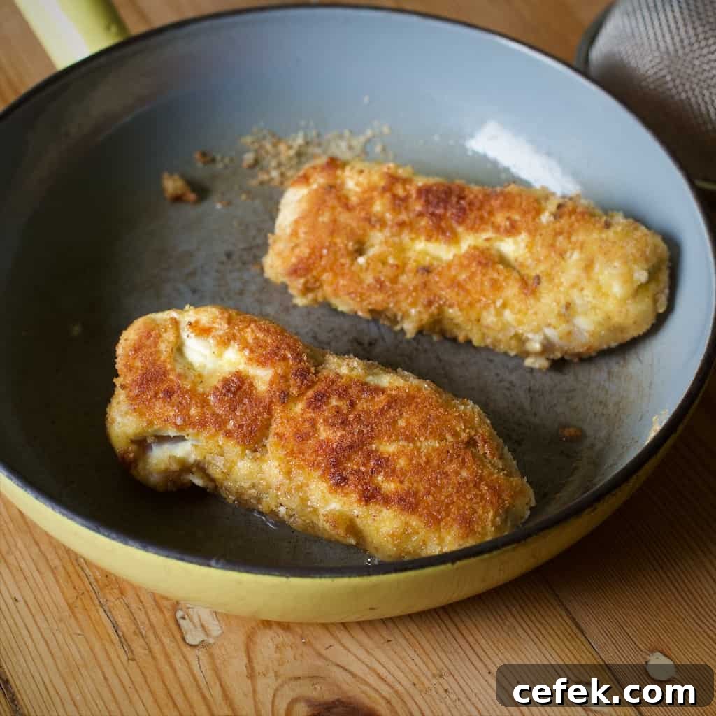 Small frying pan on a wooden kitchen counter containing two golden brown chicken Kiev