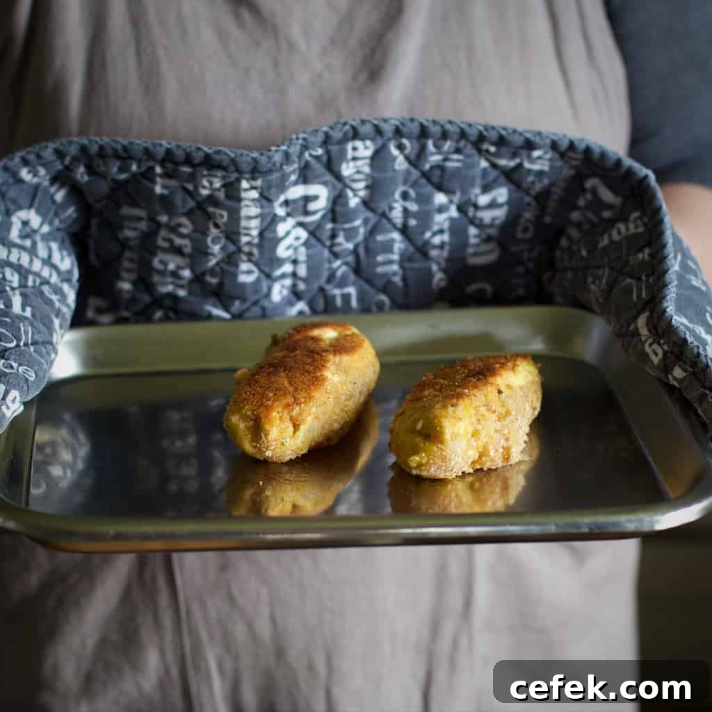 Woman holding a silver baking tray with two small golden brown chicken kievs on