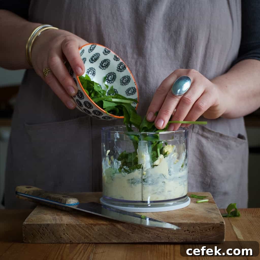 Woman tipping green wild garlic leaves into a small food processor bowl with butter