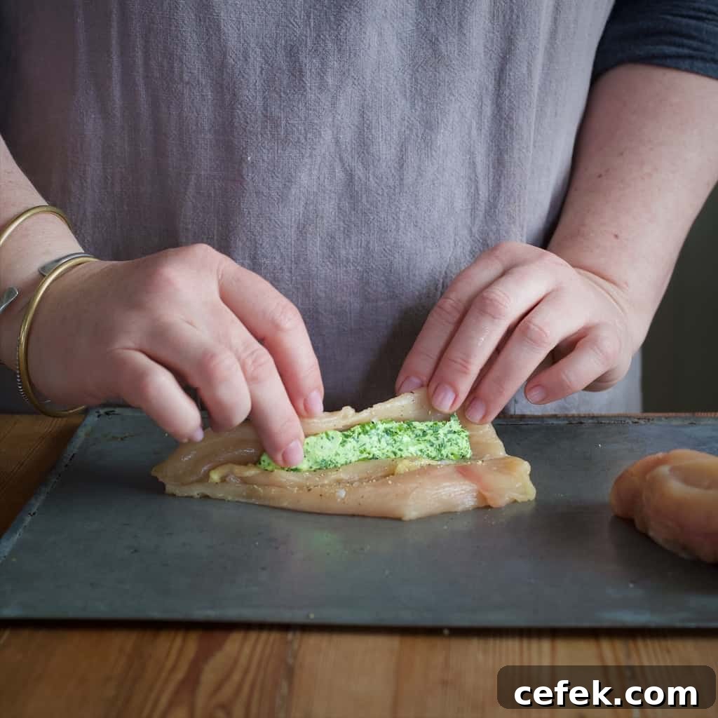 Woman in grey rolling a butterflied chicken breast around a piece of bright green wild garlic butter to make a homemade chicken Kiev