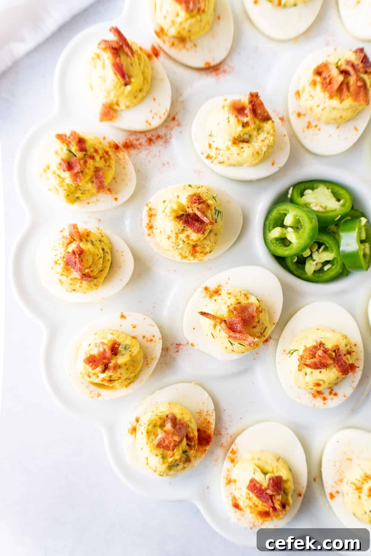 jalapeno deviled eggs with bacon garnish on a white platter with fresh jalapenos slices.