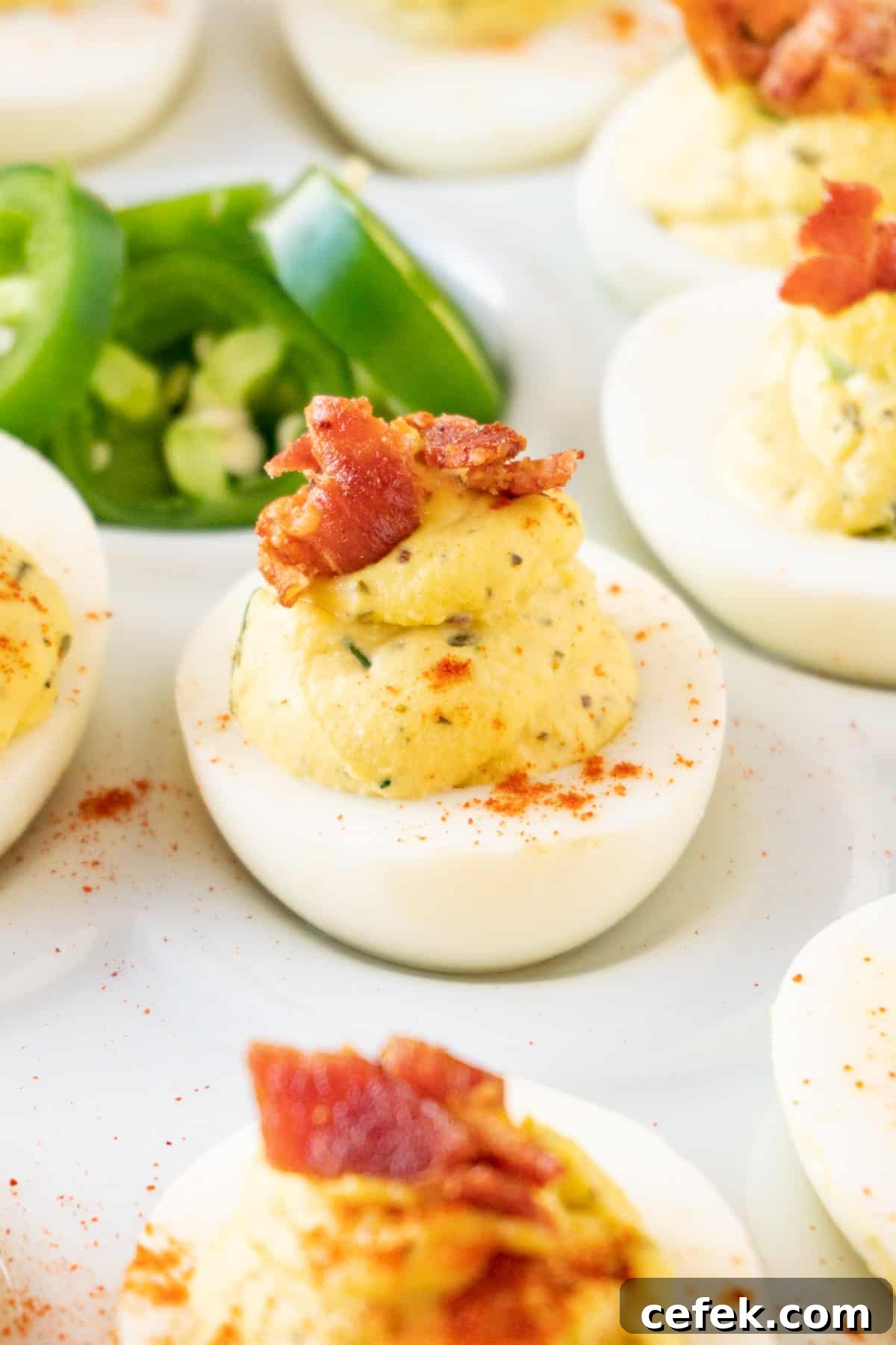 jalapeno deviled egg with bacon garnish on a white tray with jalapenos in the center.
