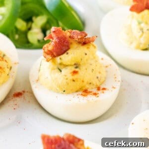 jalapeno deviled egg with bacon garnish on white platter with fresh jalapeno slices in background.