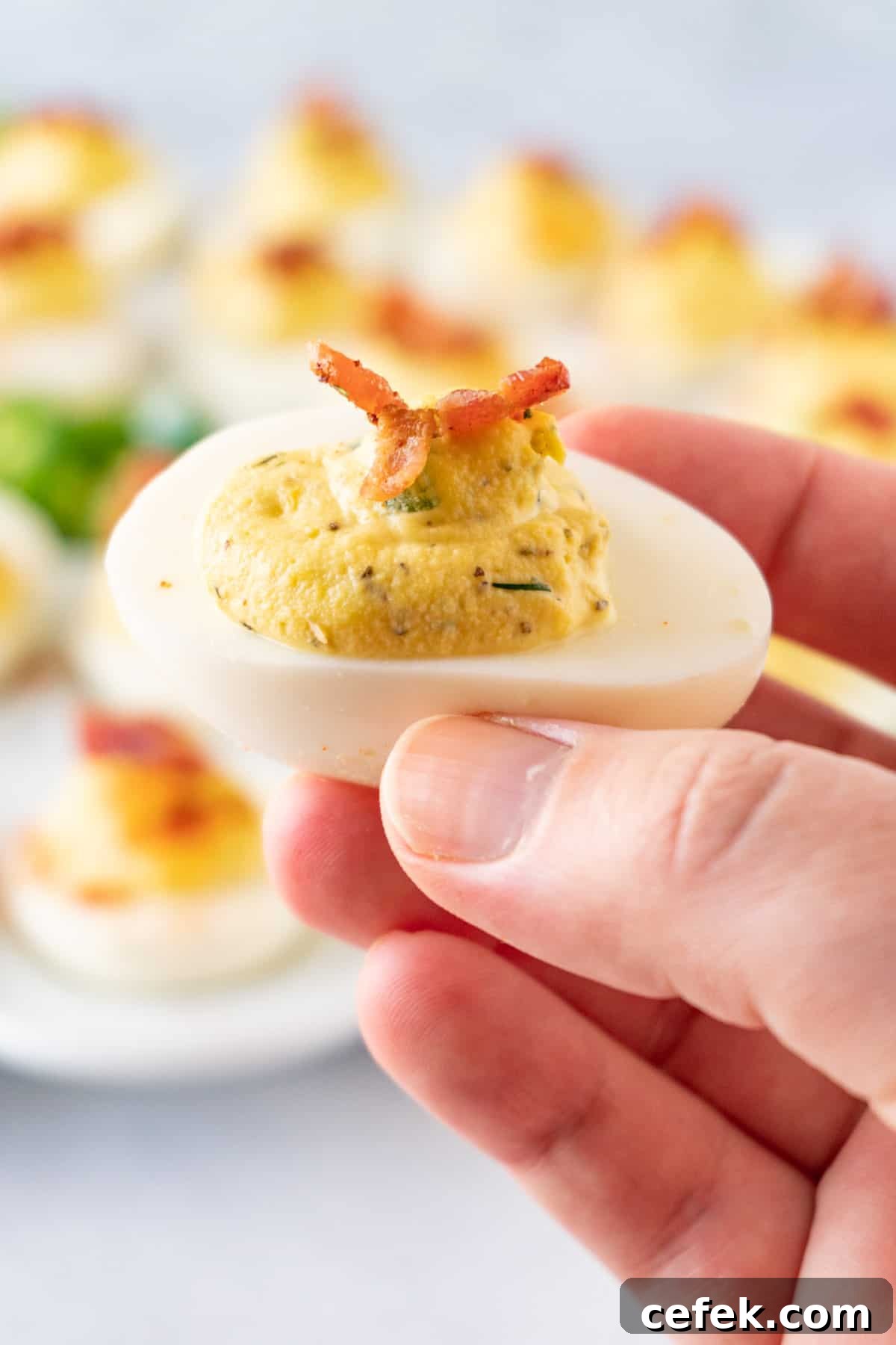 holding a jalapeno deviled egg with bacon garnish.