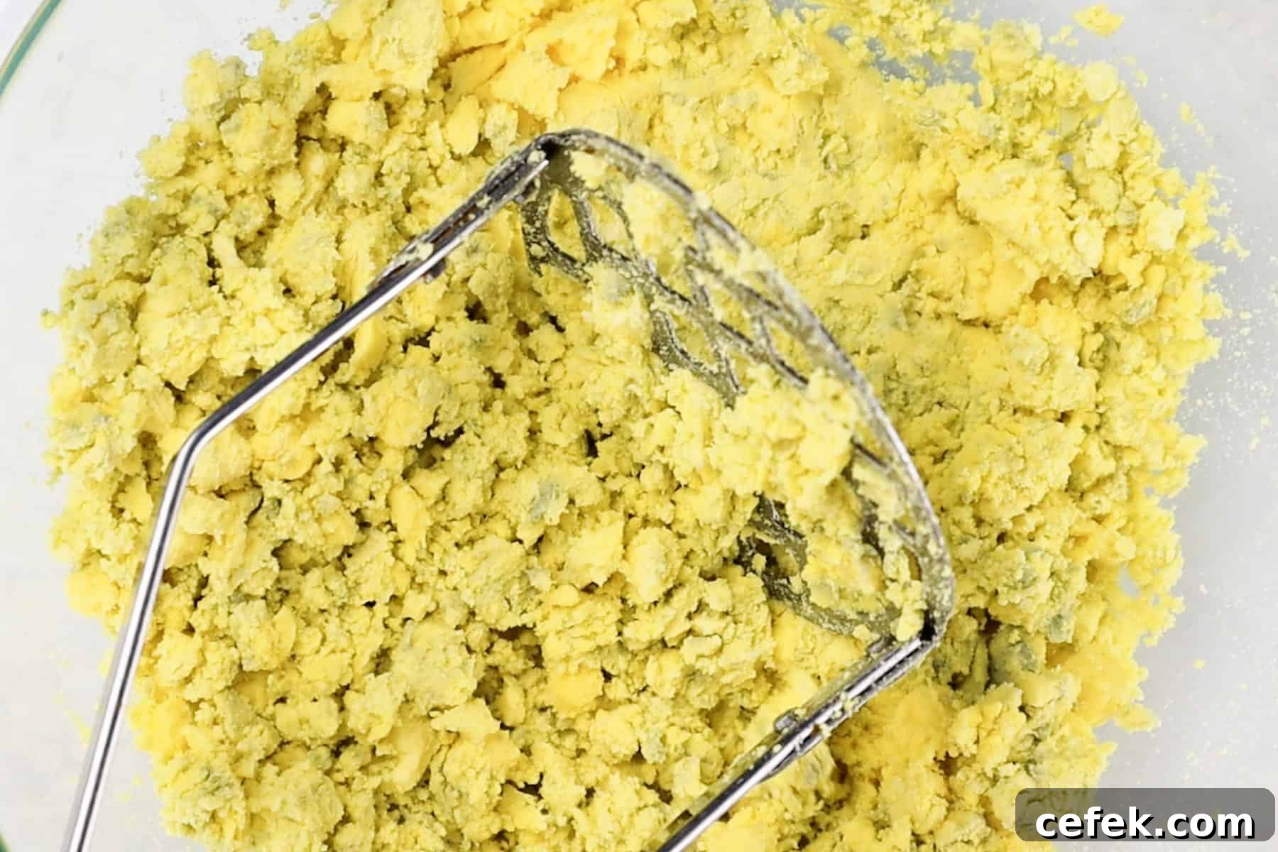 mashed egg yolks in a glass bowl with potato masher.