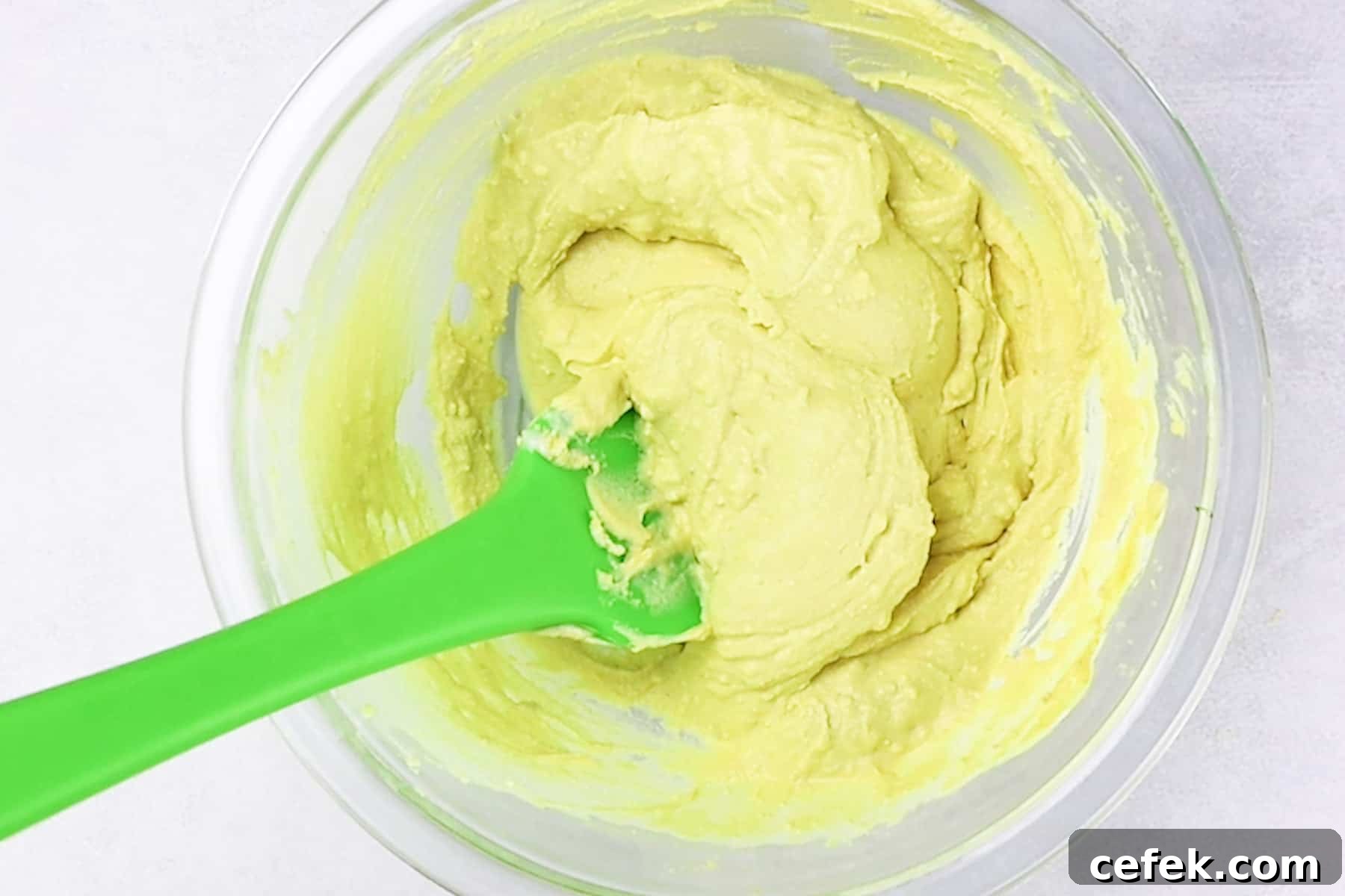 creamy egg yolk mixture in a bowl with a green spatula.