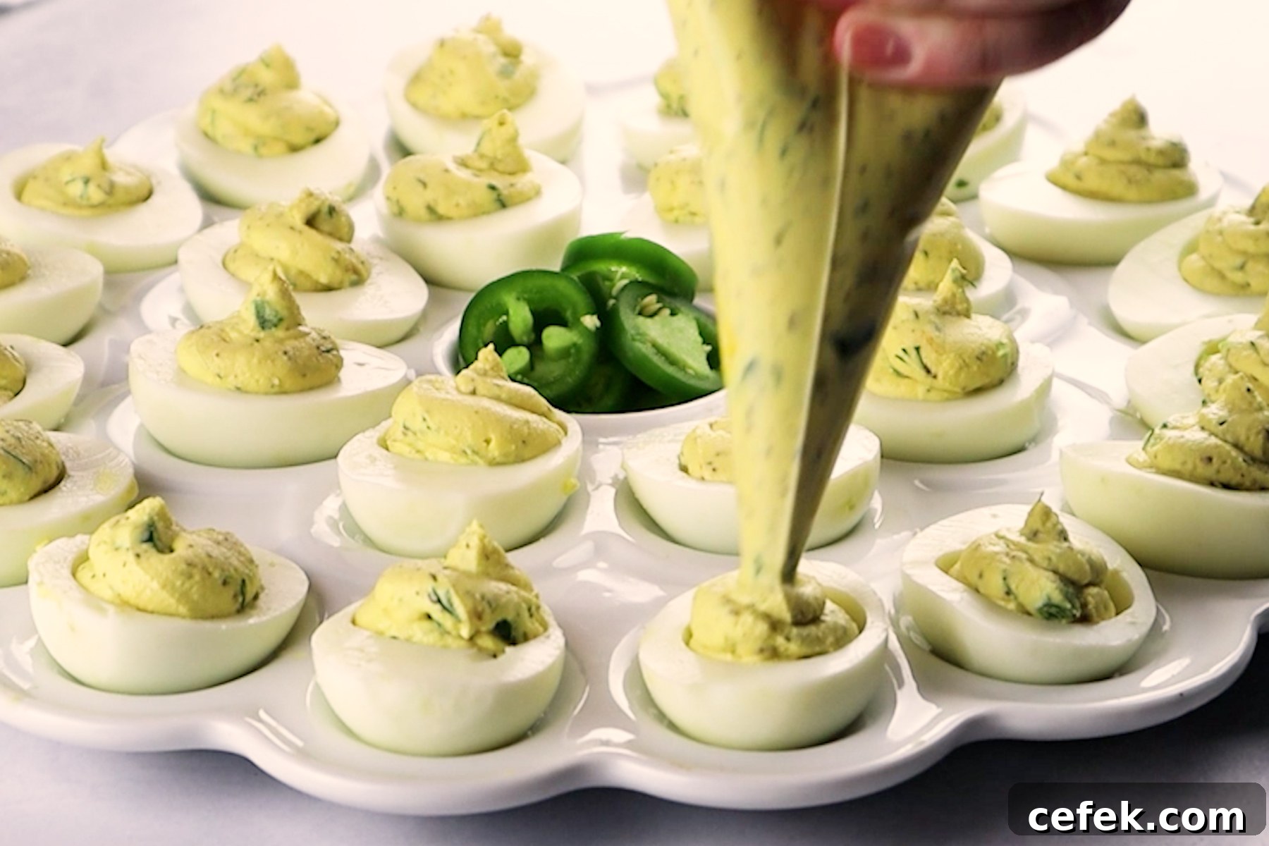 piping filling into egg whites sitting on a white platter.