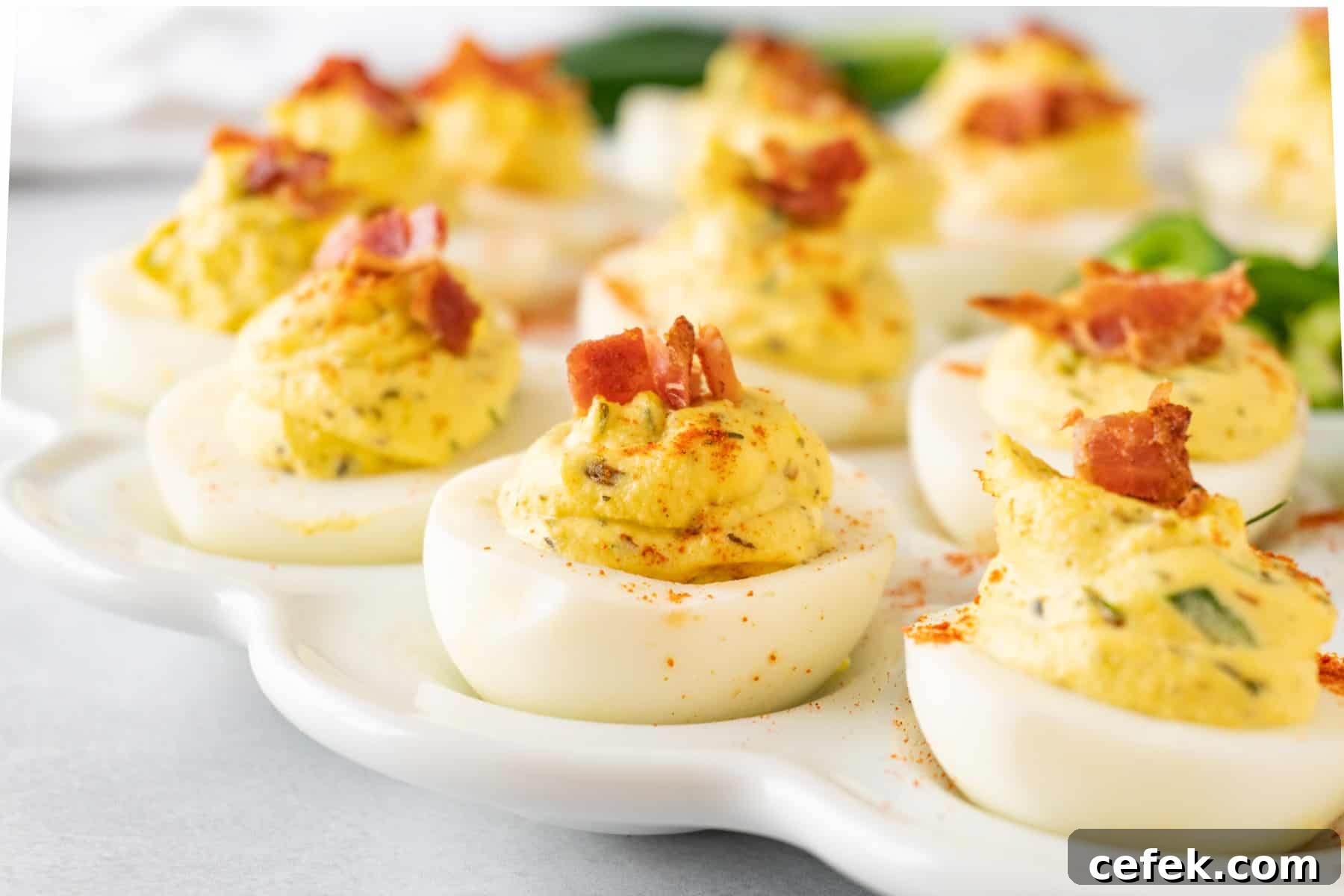 deviled eggs on a white platter with bacon as garnish.