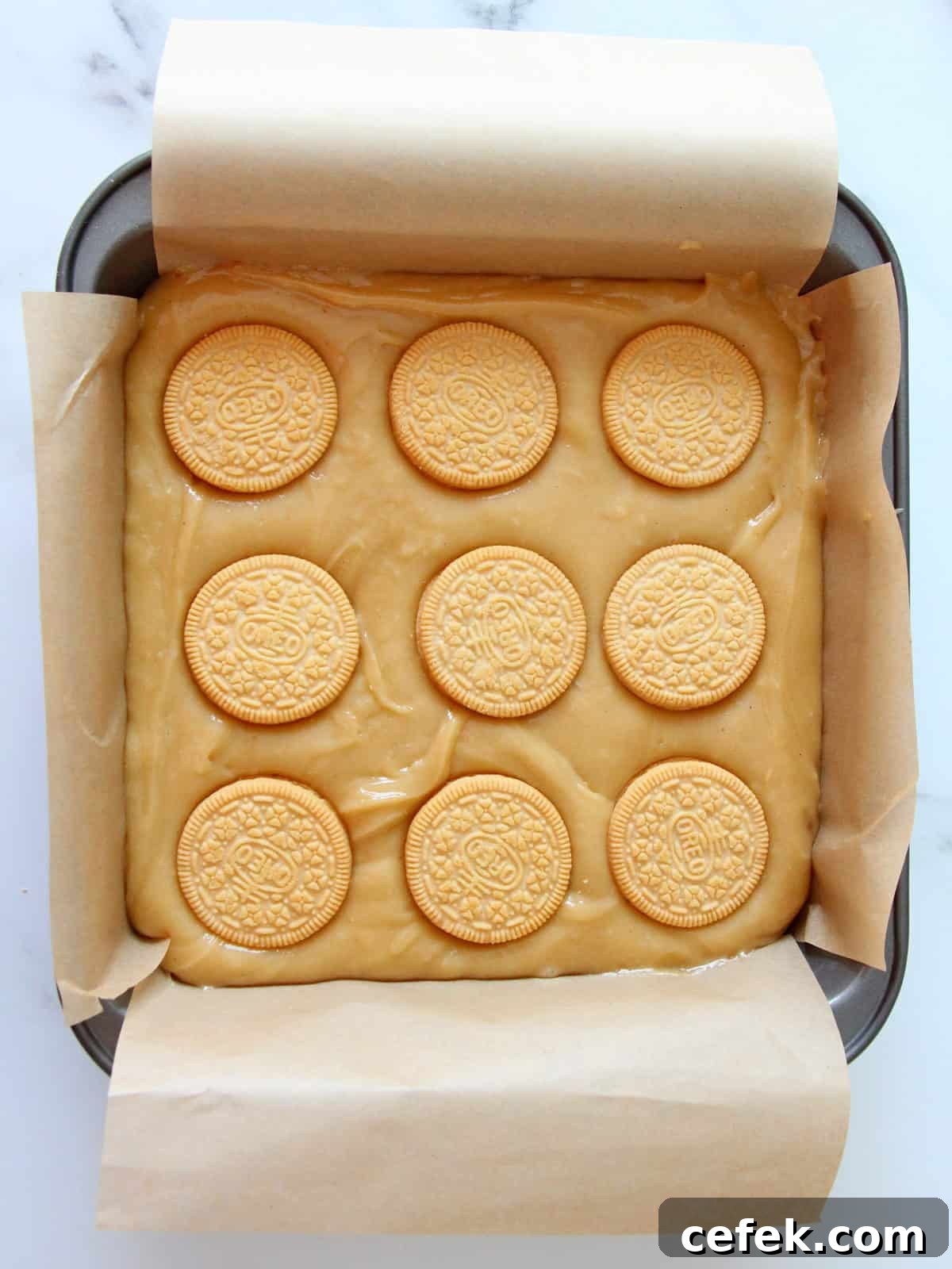 Fresh batter for oreo blondies spreaded in the pan and topped with nine golden oreo cookies