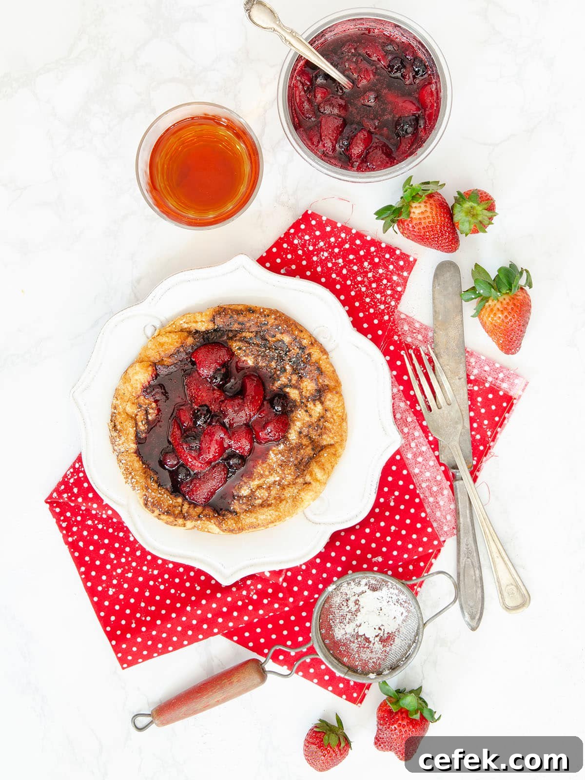 Top down view of the matzo meal pancake on a white plate with fruit compote on top and a cup of tea on the side.