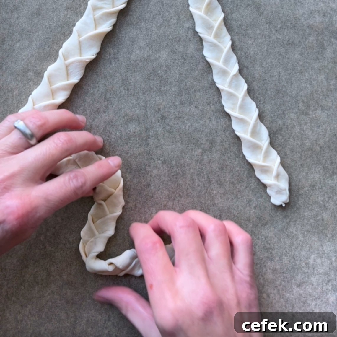 Two hands shape a strip of braided dough on a parchment-lined surface.