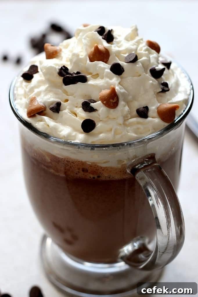 Side shot of peanut butter hot chocolate in glass mug with whipped topping and chocolate chips.