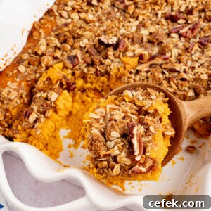 A spoon scoops out a serving of sweet potato casserole from a white rectangular baking dish.