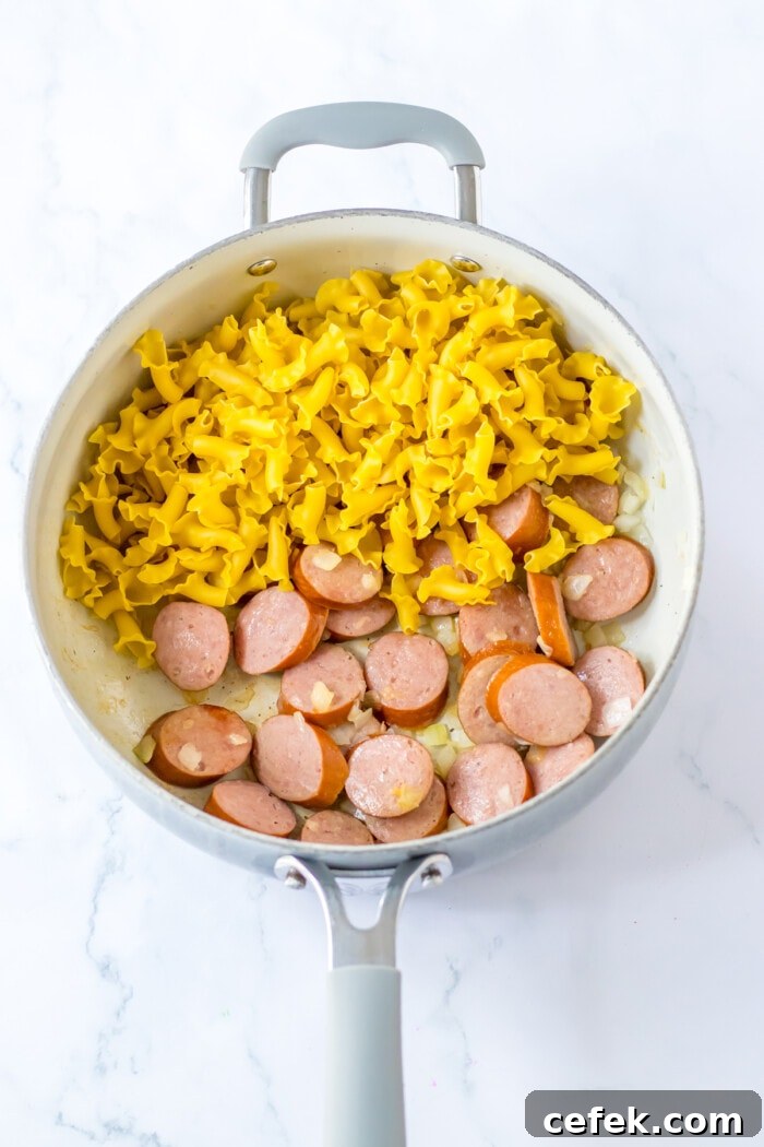 pasta in skillet with cooked sausage and onions