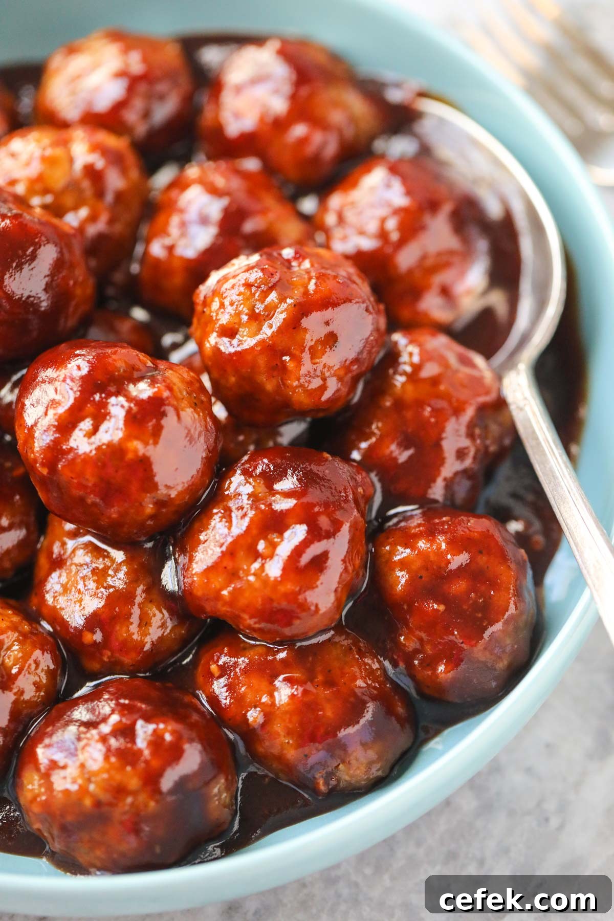 Cranberry meatballs in a blue serving bowl with a silver serving spoon.