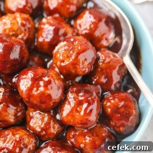 Cranberry meatballs in a blue serving bowl with a silver serving spoon.