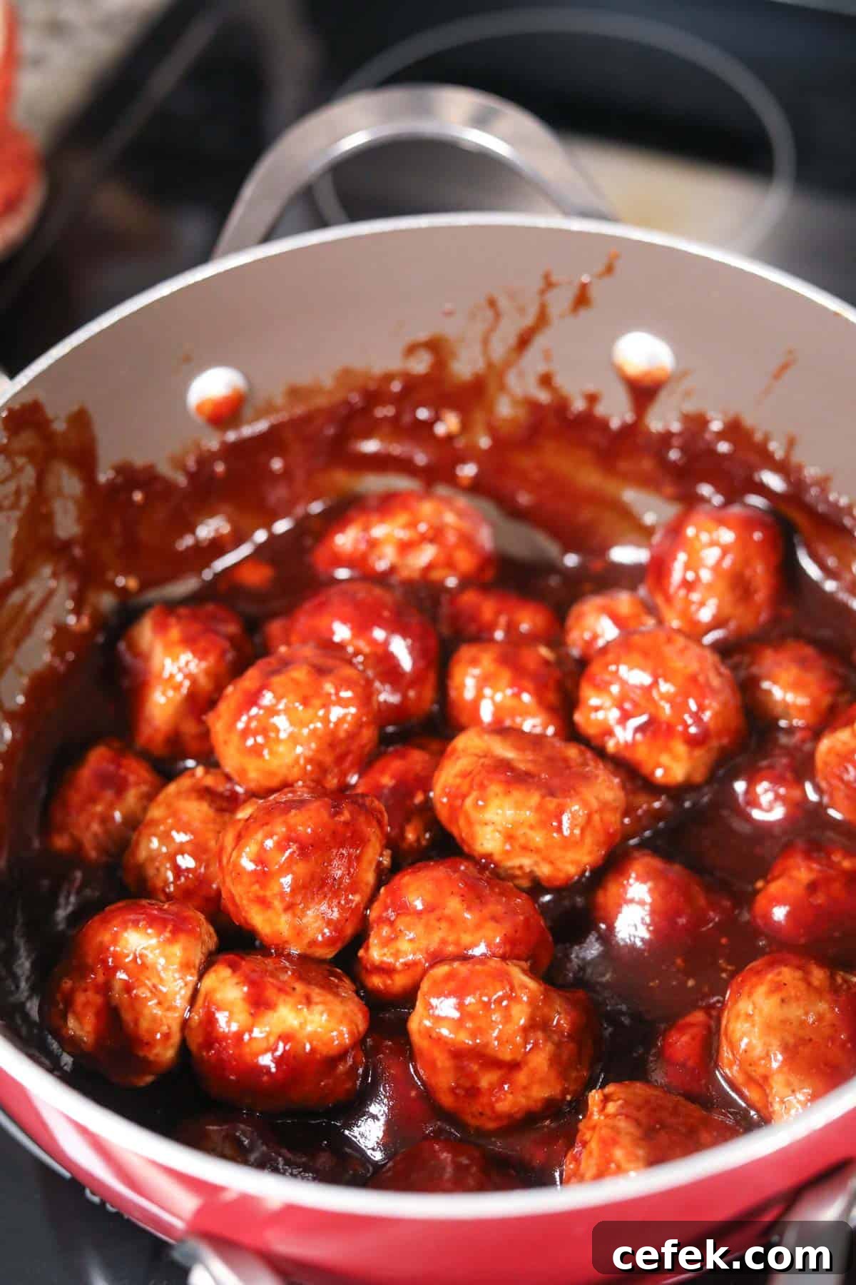 Cooked cranberry meatballs with sauce in a large sauce pan on a stove top.