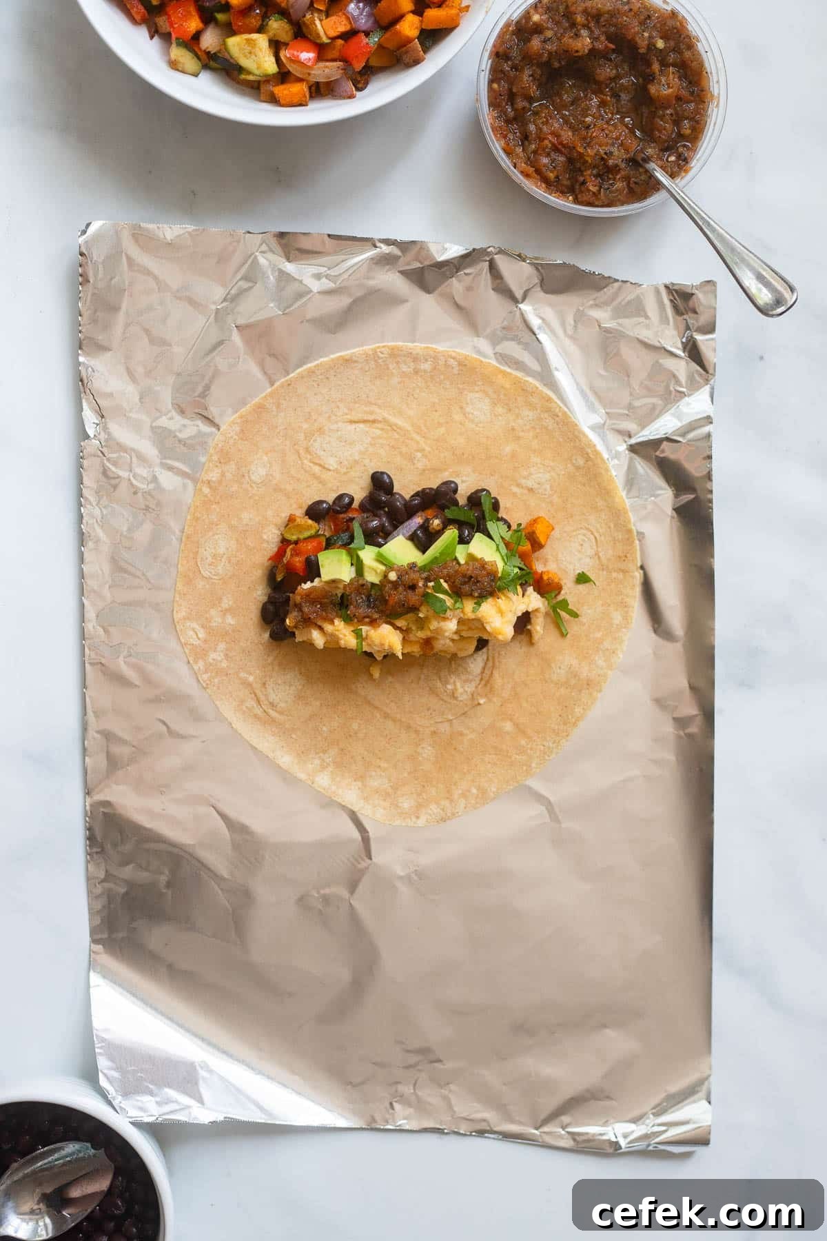 burrito laid out on a sheet of aluminum foil with fillings in tortilla before wrapping.