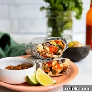 healthy breakfast burrito wrapped in foil on a pink plate.