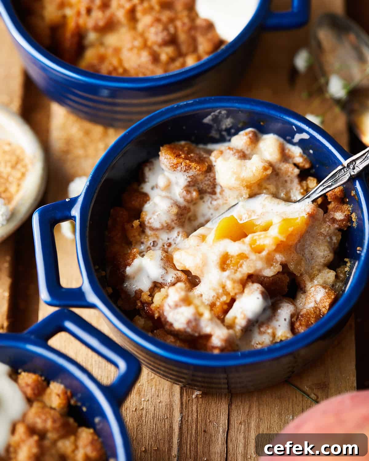 Spoon breaking into air fryer peach cobbler with whipped cream.