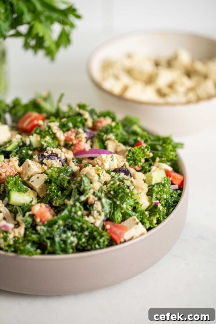 Bowl of kale salad with quinoa, tofu, tomato, cucumber and red onion. Tofu in background.