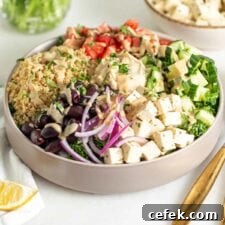 Adding a spoonful of tahini to a olorful bowl of quinoa, chopped tomato and peppers, red onion, olives and tofu.