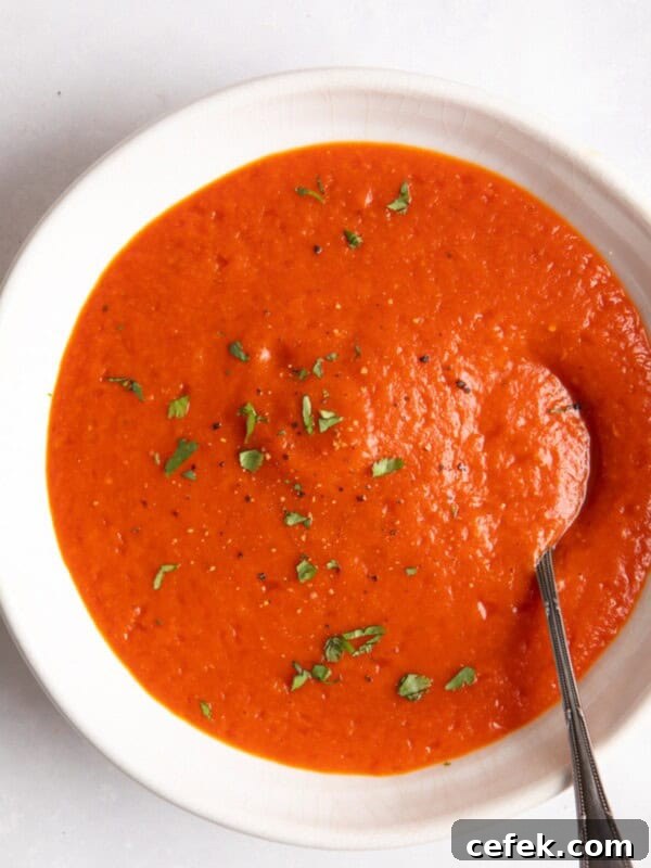 red pepper and tomato soup served in a white bowl with a spoon inside.