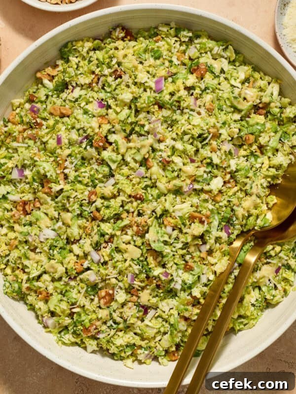 Brussels sprout salad in bowl with serving utensils, topped with shredded parmesan cheese.