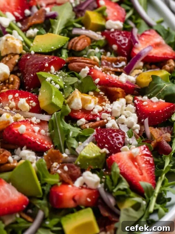 Strawberry arugula goat cheese salad on white serving plate topped with balsamic dressing.