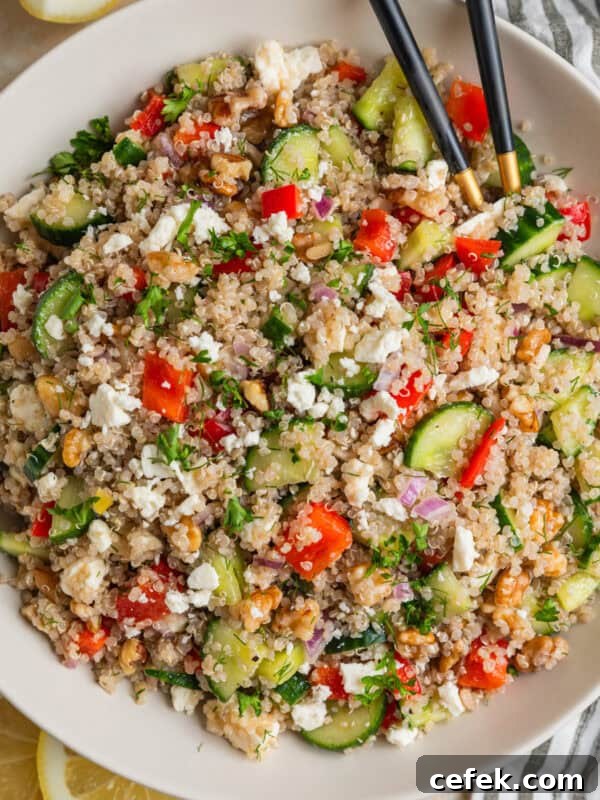 Cucumber quinoa salad in bowl with peppers, feta, chopped dill and serving utensils.