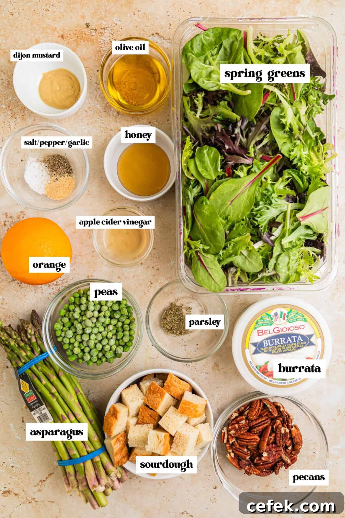 Mixed greens, bread cubes, burrata cheese, asparagus and other salad ingredients arranged on surface.