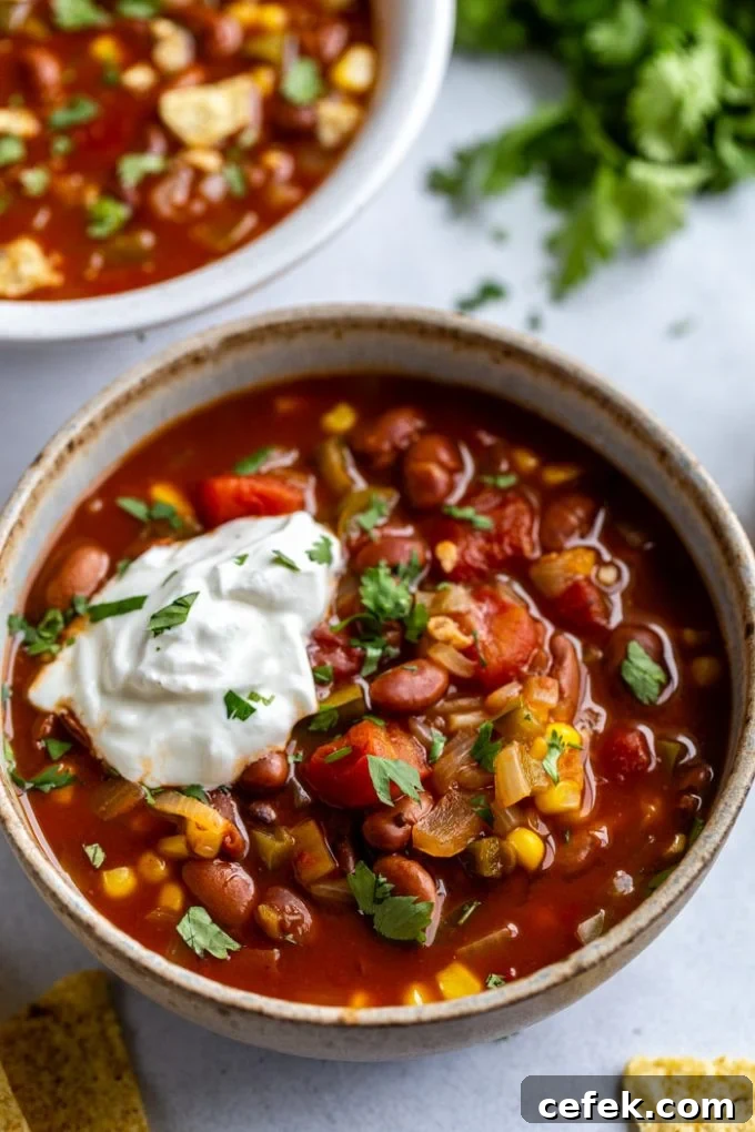 bowl of vegetarian chili with lots of tomatoes and beans. topped with sour cream and cilantro