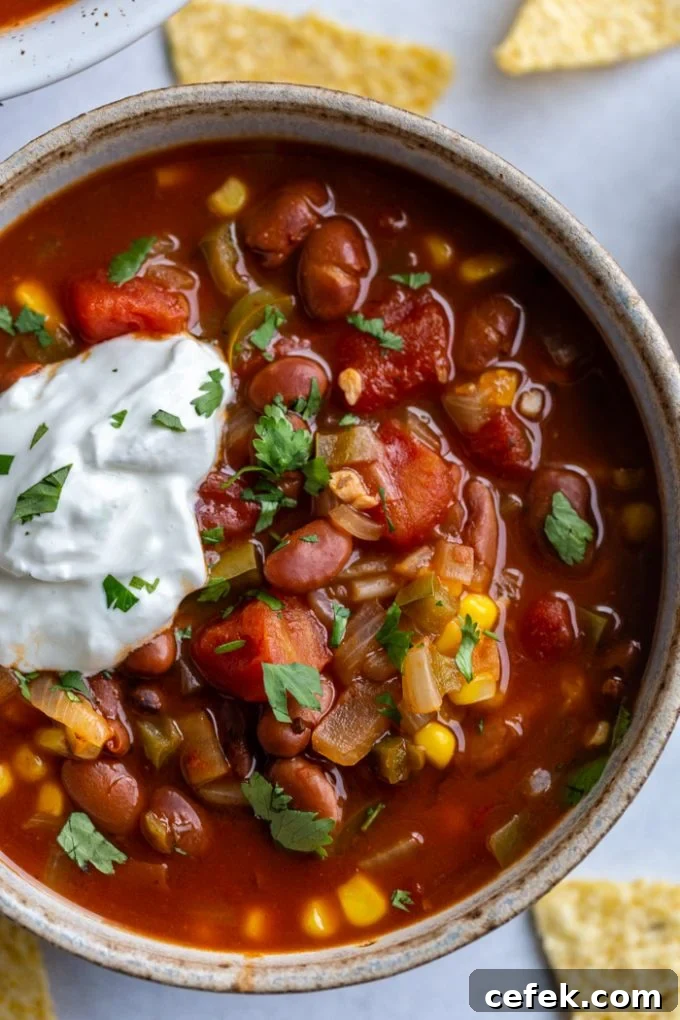 bowl of vegetarian chili with lots of tomatoes and beans. topped with sour cream and cilantro
