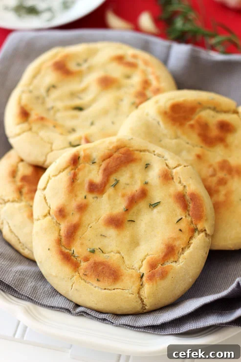 4 Gluten Free Rosemary and Garlic Flatbread rounds sitting on a gray napkin, topped with fresh rosemary.