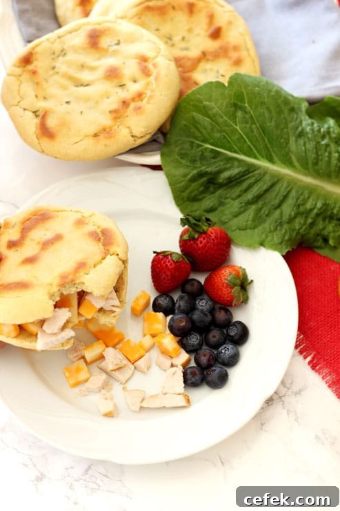 Sliced Rosemary and Garlic Flatbread pita filled with turkey and cheese with a bite taken out, side of blueberries, strawberries and lettuce.