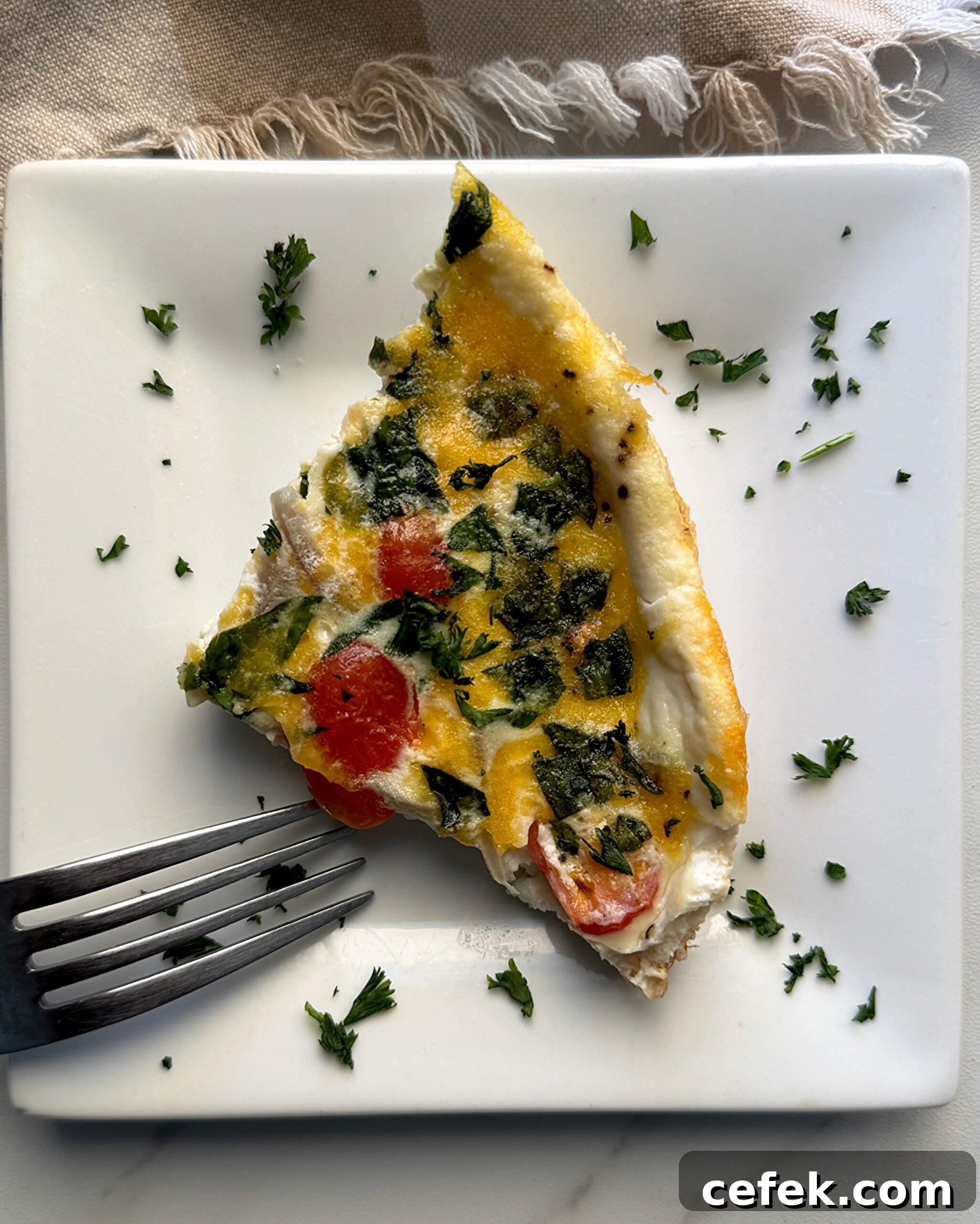 overhead shot of a slice of Slow Cooker Egg White Fritatta on a white plate garnished with fresh parsley
