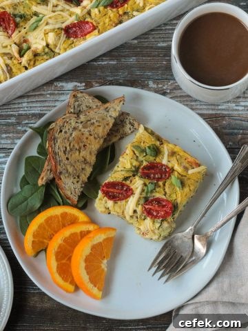 Slice of vegan breakfast casserole on a plate with toast, orange slices, and two forks.