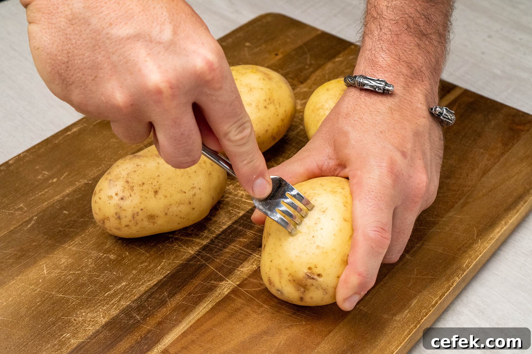 Poke holes into four potatoes on a wooden chopping board with a fork