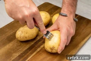 Pricking holes into four potatoes on a wooden chopping board with a fork
