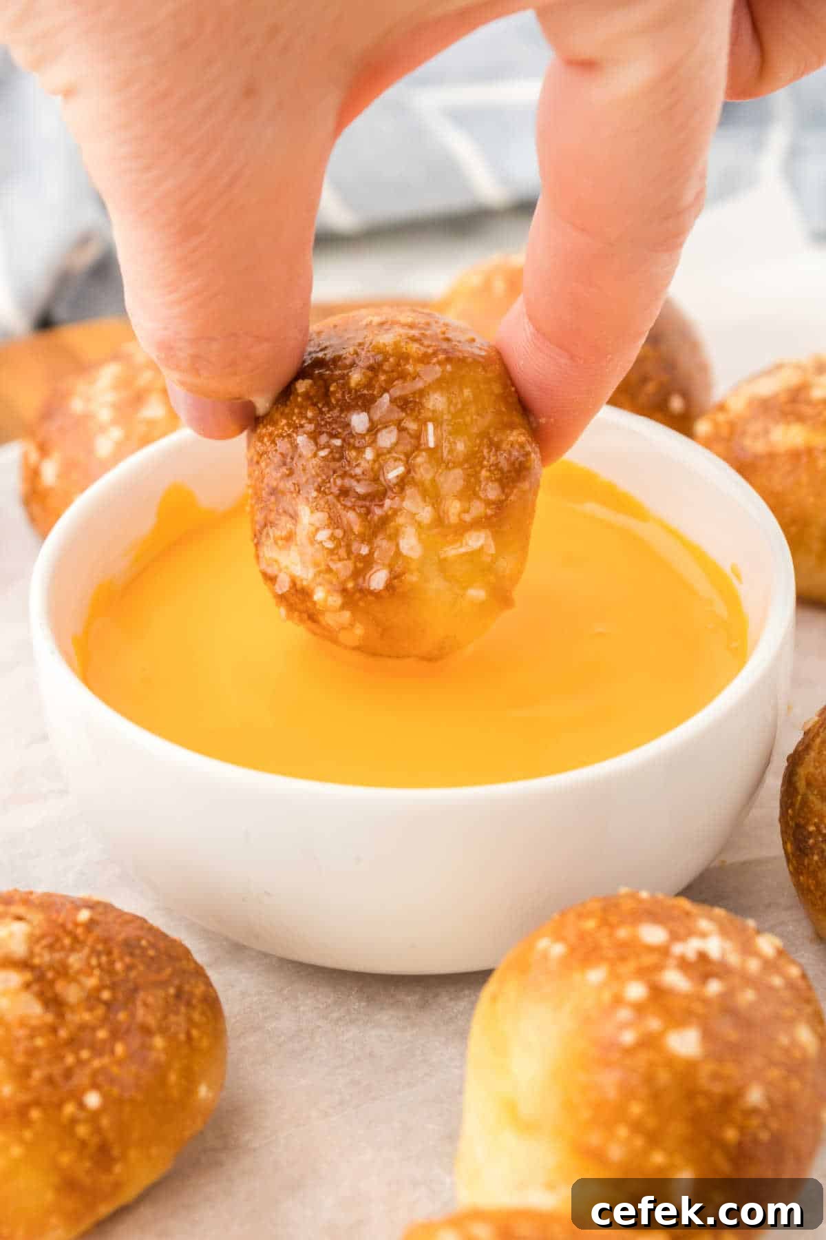 A hand dipping the recipe into cheese sauce.