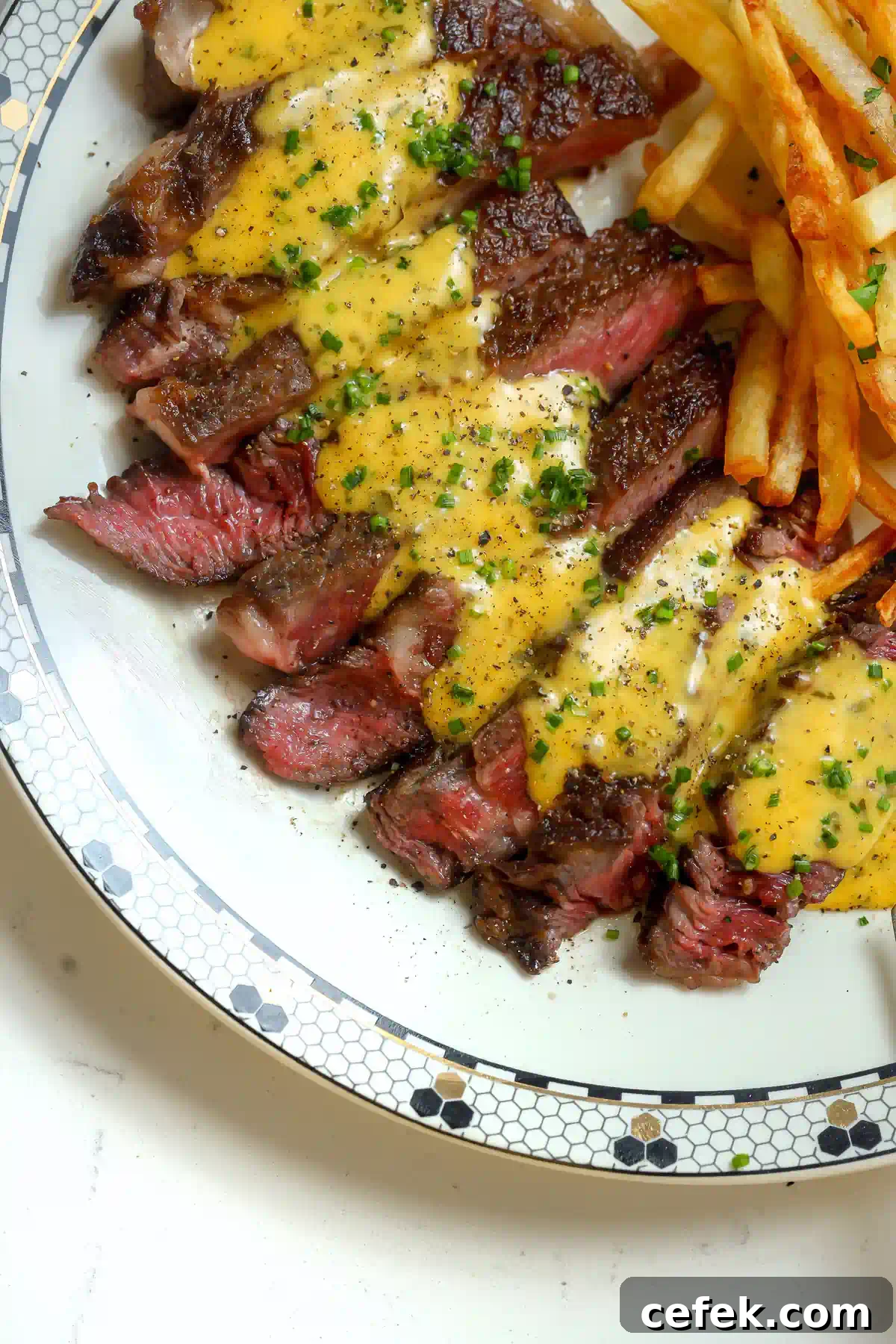 Vertical top-down view of sliced ribeye steak showing a pink center and a thick coating of velvety yellow bearnaise sauce and chopped chives.
