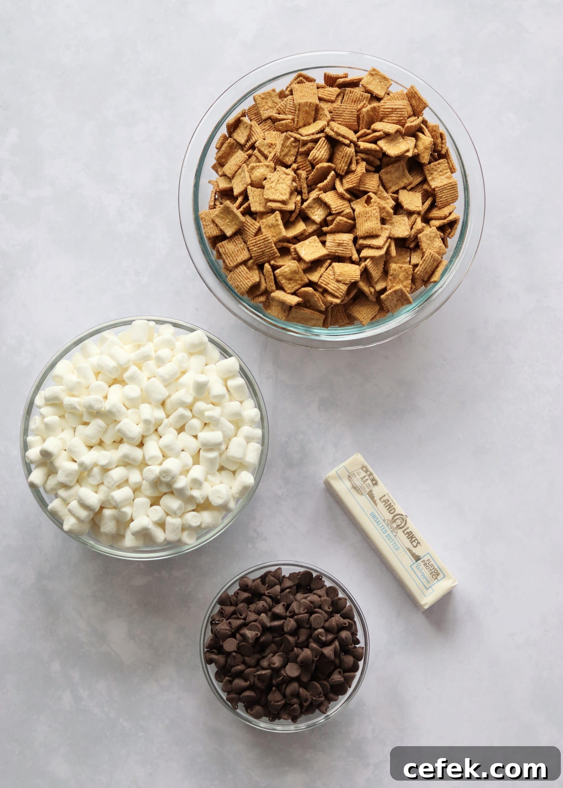S'mores bars ingredients laid out. Cereal, marshmallows, chocolate chips, and a stick of butter.