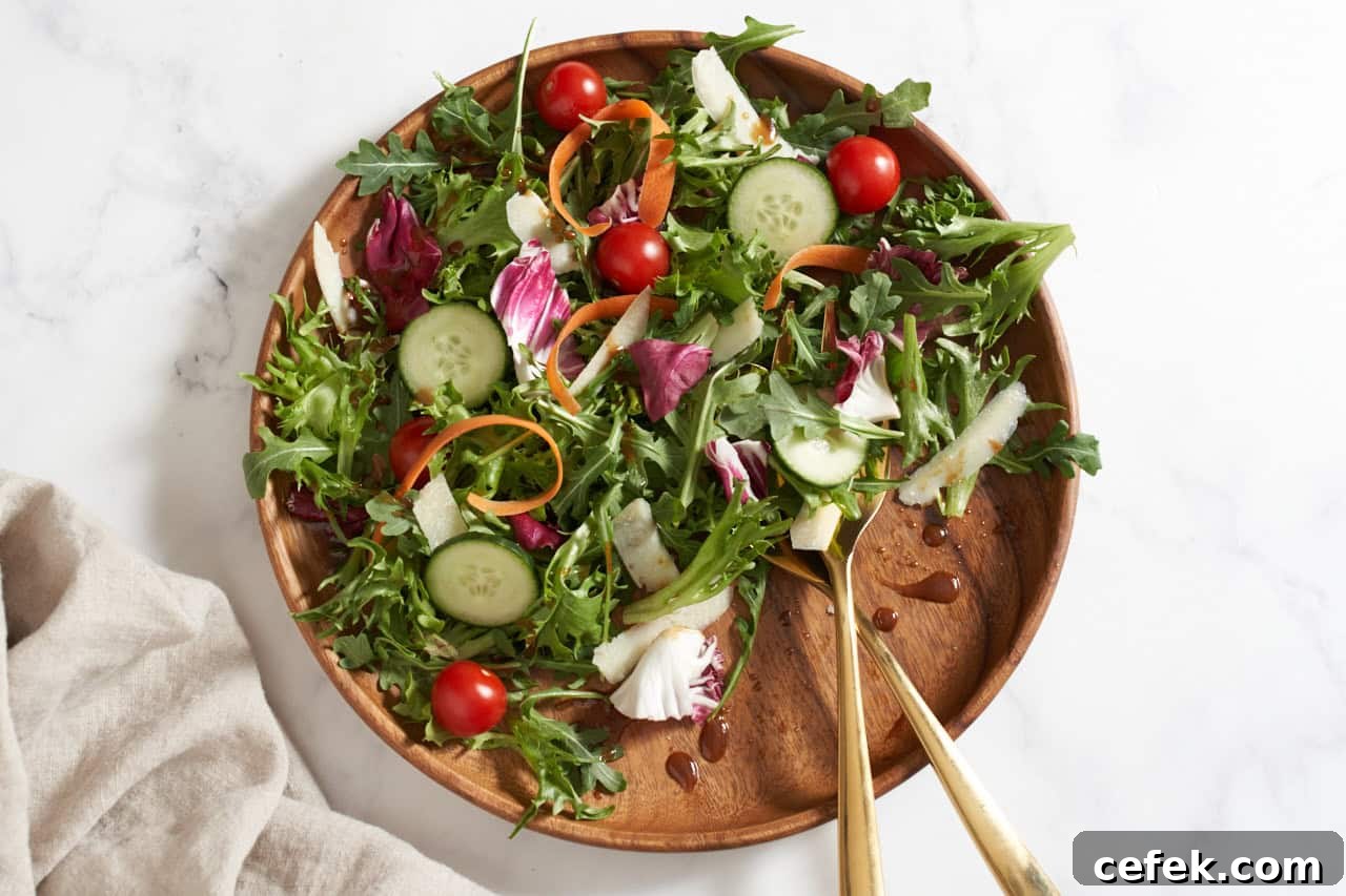 An insalata mista on a wooden plate with gold serving utensils.