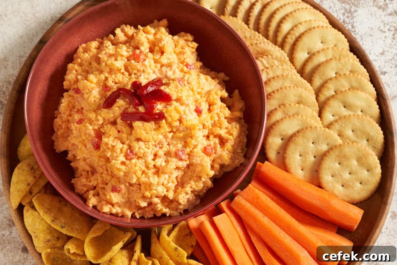 Pimento cheese dip in a red bowl on a wooden tray.
