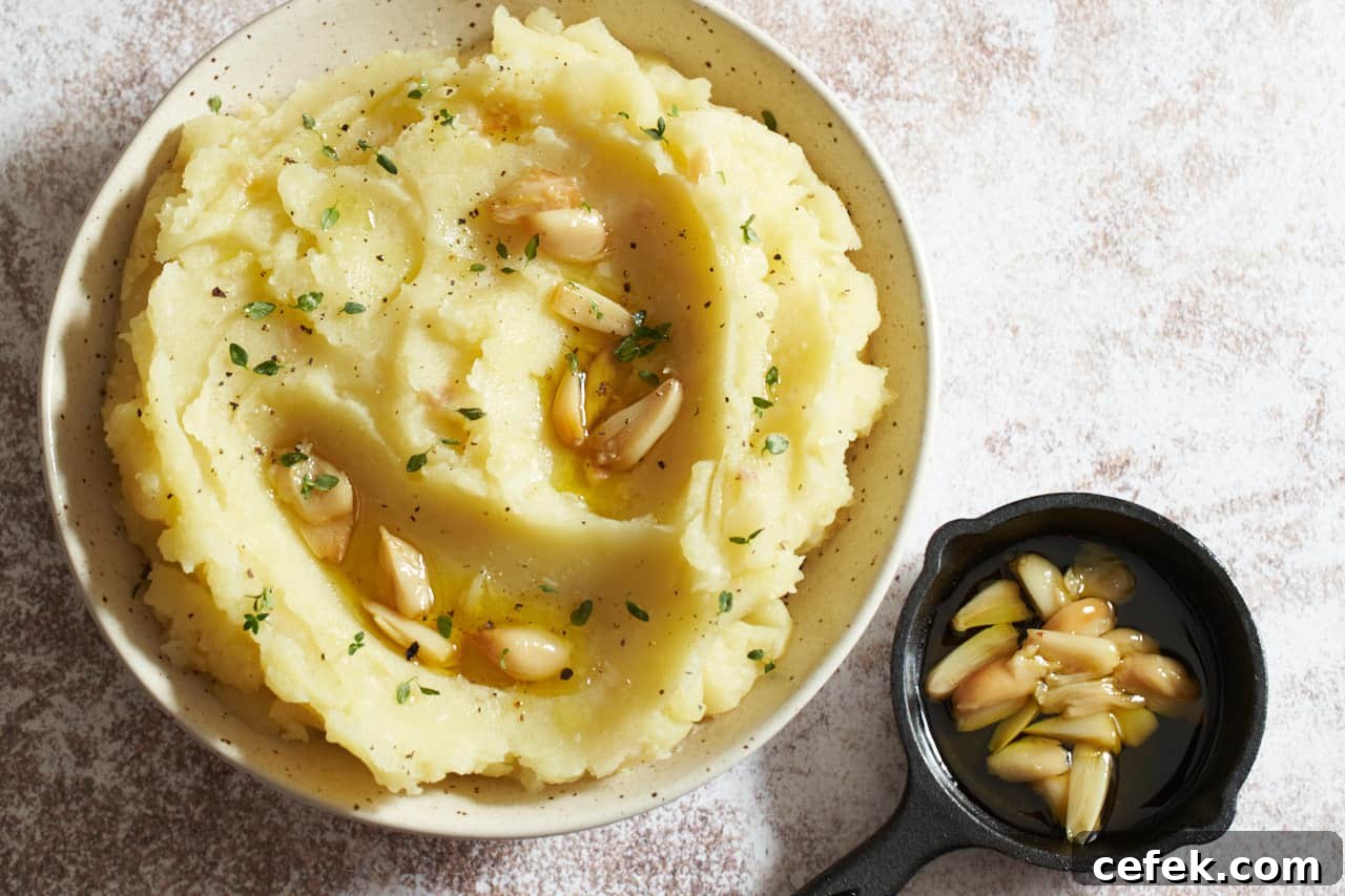 A bowl of mashed potatoes topped with roasted garlic cloves and fresh thyme.