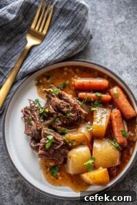 white plate with serving of pot roast, carrots, potatoes and gravy topped with parsley