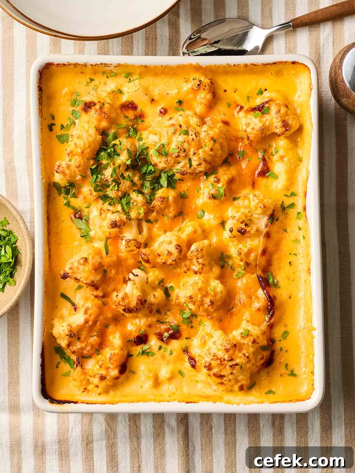 An oven dish filled with baked Cauliflower Cheese on a table with a stripy tablecloth, ready to be served.